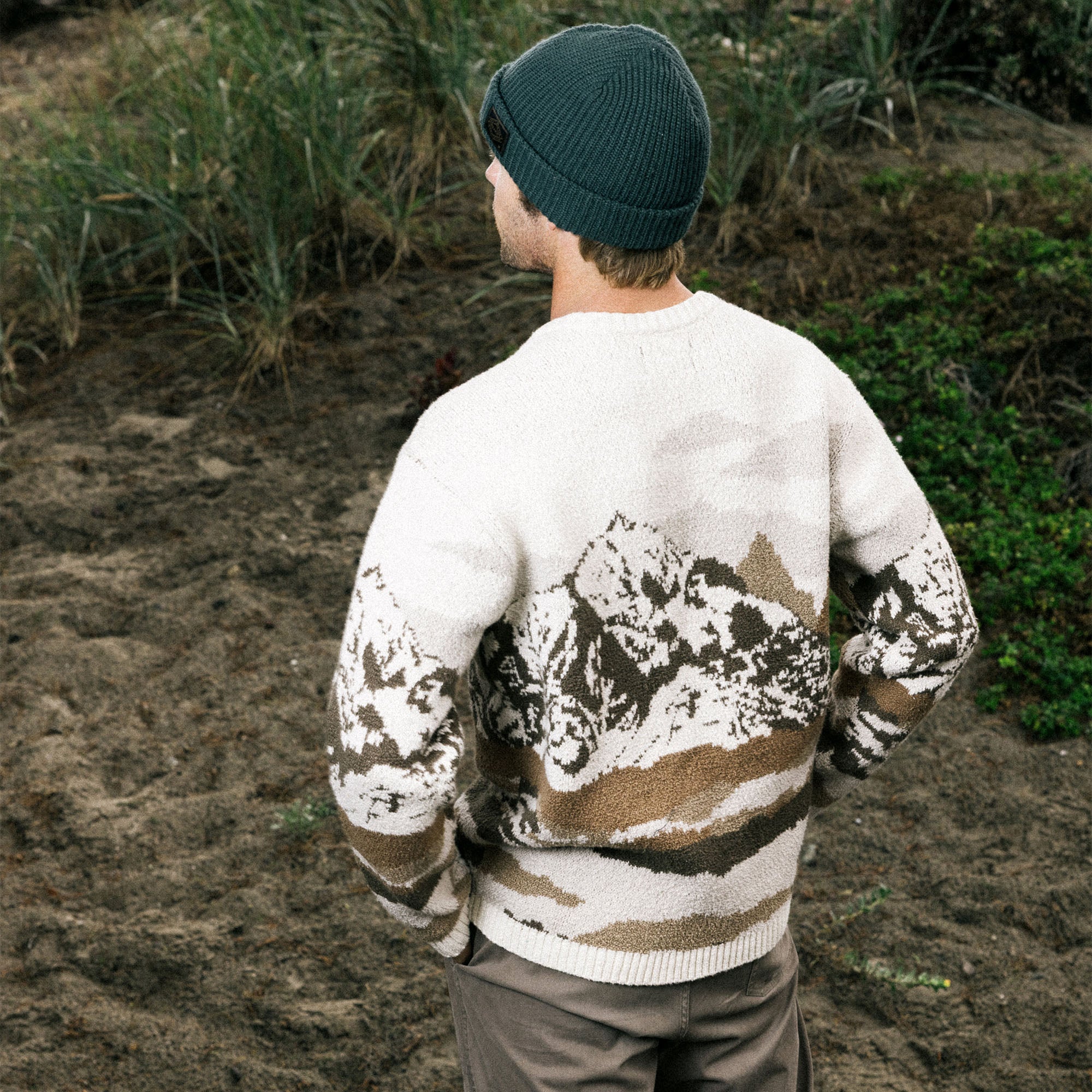 Person wearing a patterned sweater with mountains and trees, standing outdoors.
